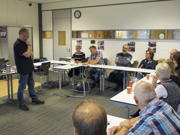 Deelnemers zitten aan een tafel en luisteren interactief naar de docent