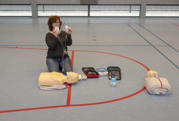 Vrouw geeft EHBO-cursus aan gymnastiekdocenten, demonstrerend in een lesomgeving.