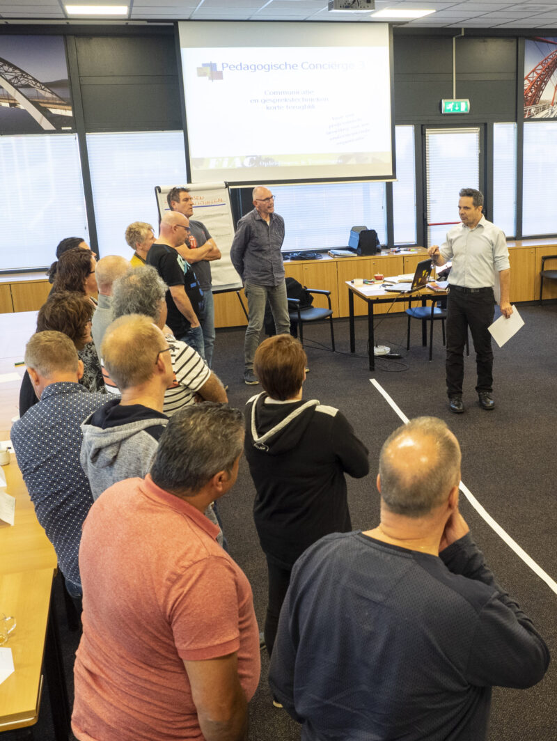 Deelnemers staan en luisteren aandachtig naar de trainer die voor hen staat